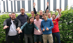 Vorstandsteam in Wolfsburg. Zu sehen 9 Vorstandsmitglieder, die vo einer Hecke posieren und freudig die Hände hoch reißen